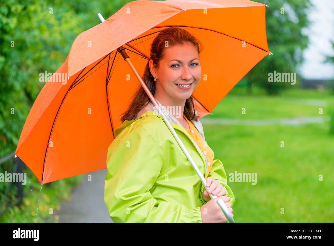 30-j hrige lächelndes Mädchen hält ein Dach unter dem Regen Stockfoto