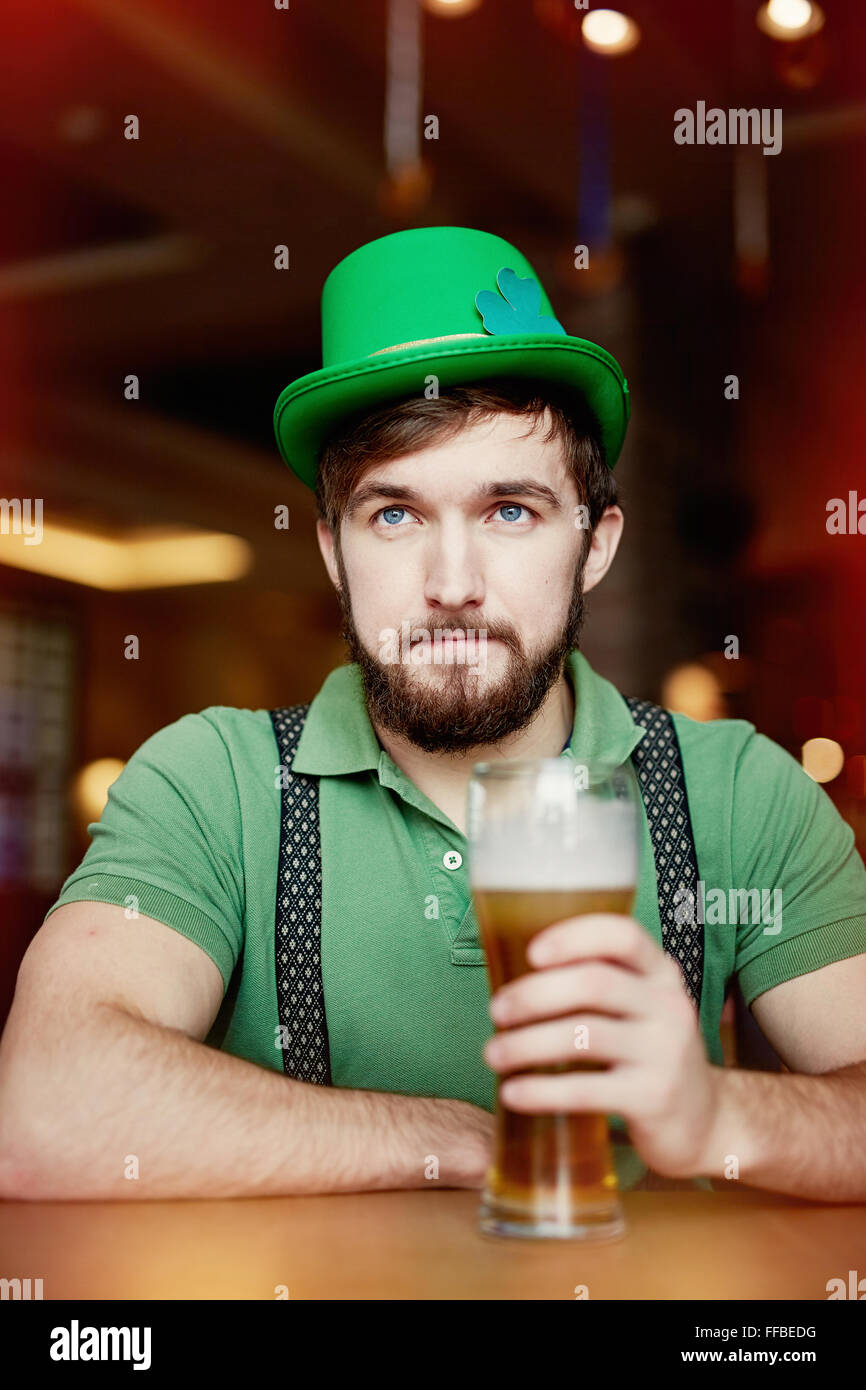 Junger Mann im grünen Hut und T-shirt im Pub mit Glas Bier sitzen Stockfoto