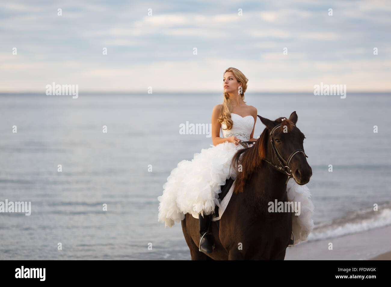 Braut auf einem Pferd am Meer in ihrem Hochzeitstag Stockfoto