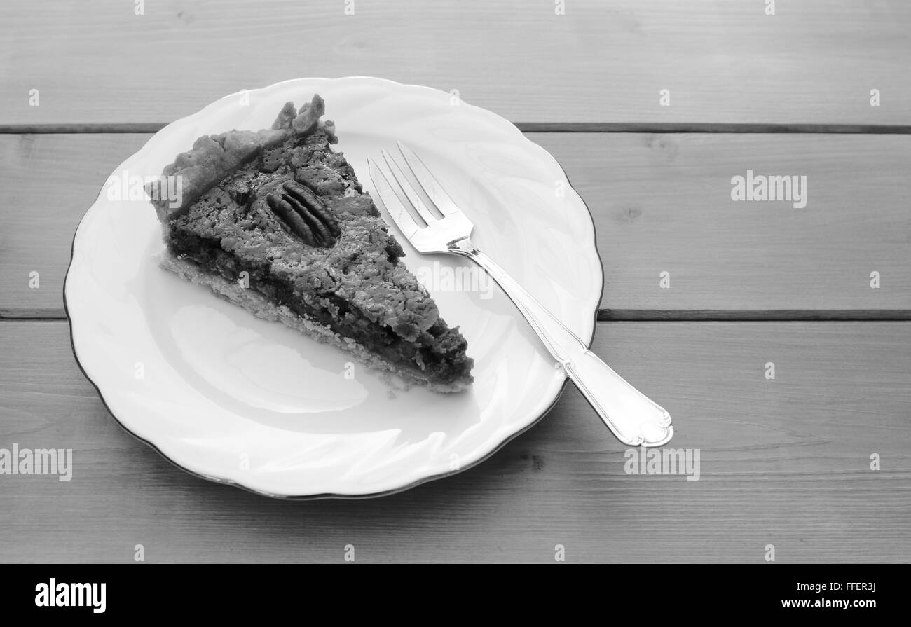 Verarbeitung von Stück frisch gebackenen Pekannuss-Torte auf einem Porzellanteller mit einem Dessertgabel - Monochrom Stockfoto