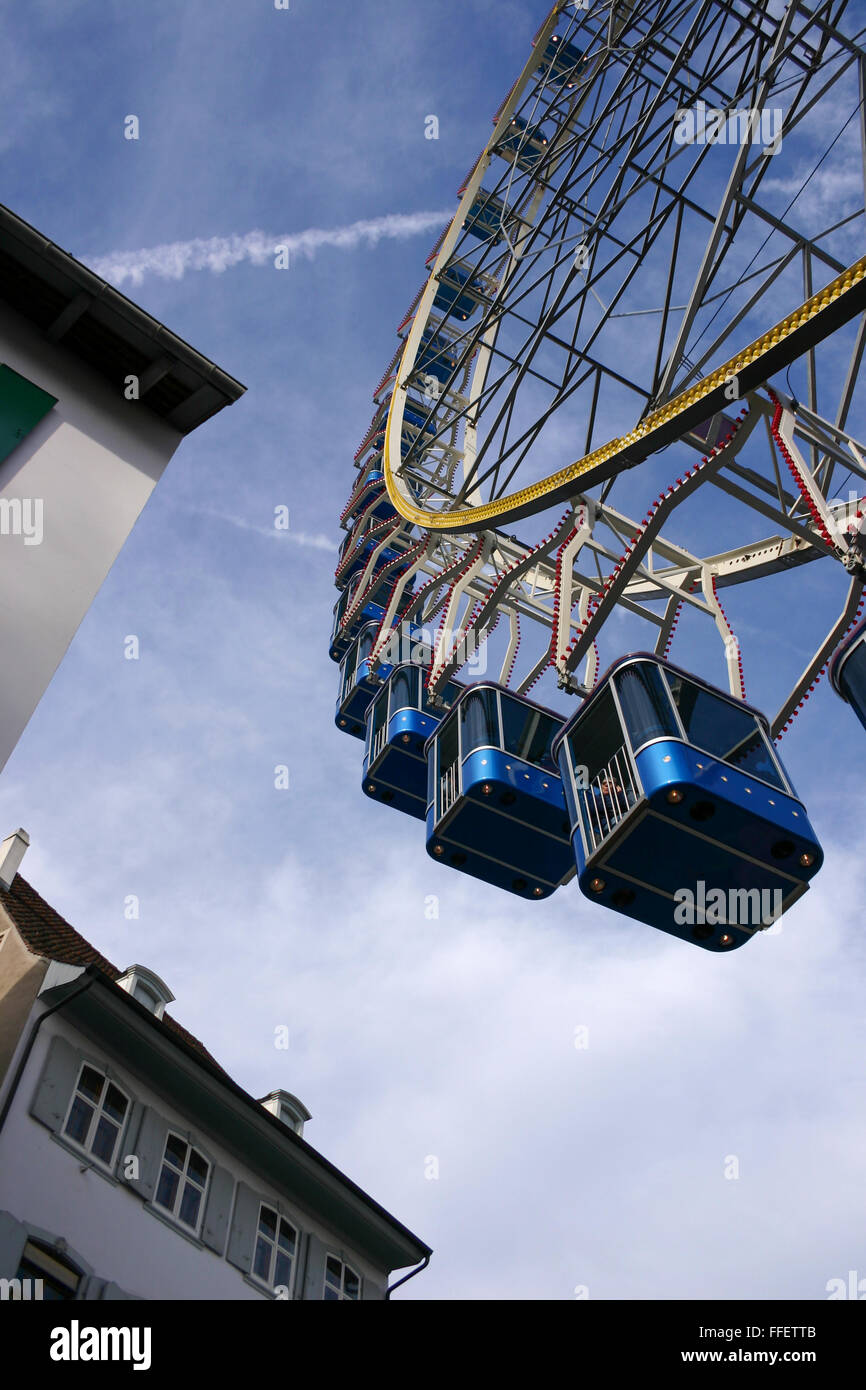 Ansicht von unten auf eine große Fähre Rad mit elektrischen blauen Kabinen über den Dächern von zwei alte Häuser Stockfoto