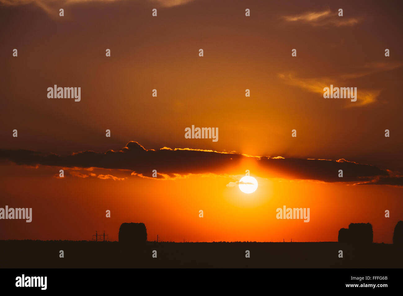 Sommer Wiese mit Heu Ballen Silhouetten unter Abendlicht. Hellen Himmel und dunklen Boden. Sonne über ländliche Landschaft Bereich Stockfoto