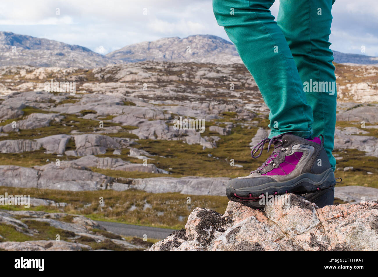 Fokus auf die Beine eines weiblichen Modell trägt lila und grau Wanderschuhe mit felsigen Landschaft im Hintergrund. Schottland, Großbritannien. Stockfoto