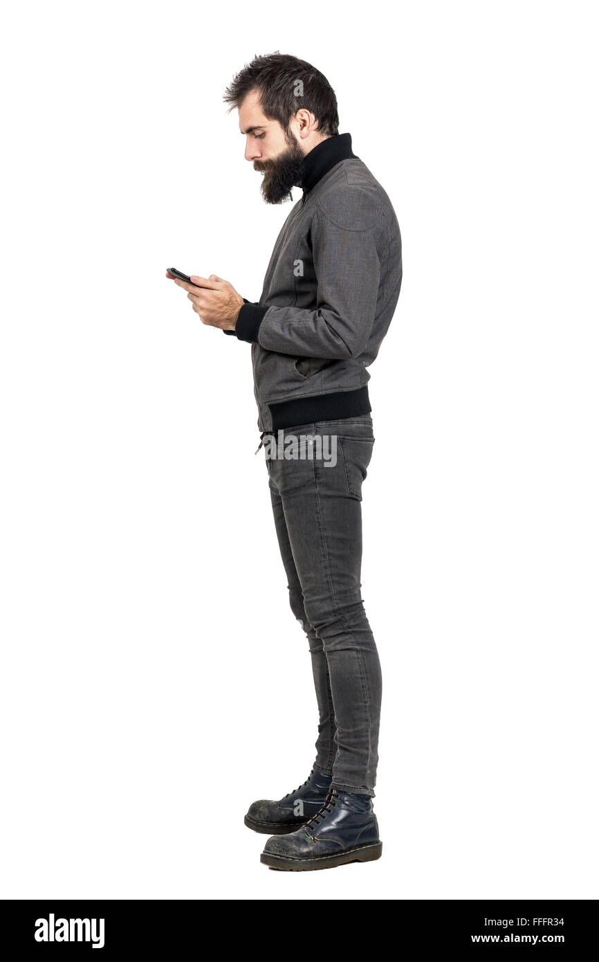 Seitenansicht des stilvollen bärtige Hipster Tippen auf seinem Smartphone. Ganzkörper-Länge-Porträt über weiße Studio-Hintergrund isoliert. Stockfoto