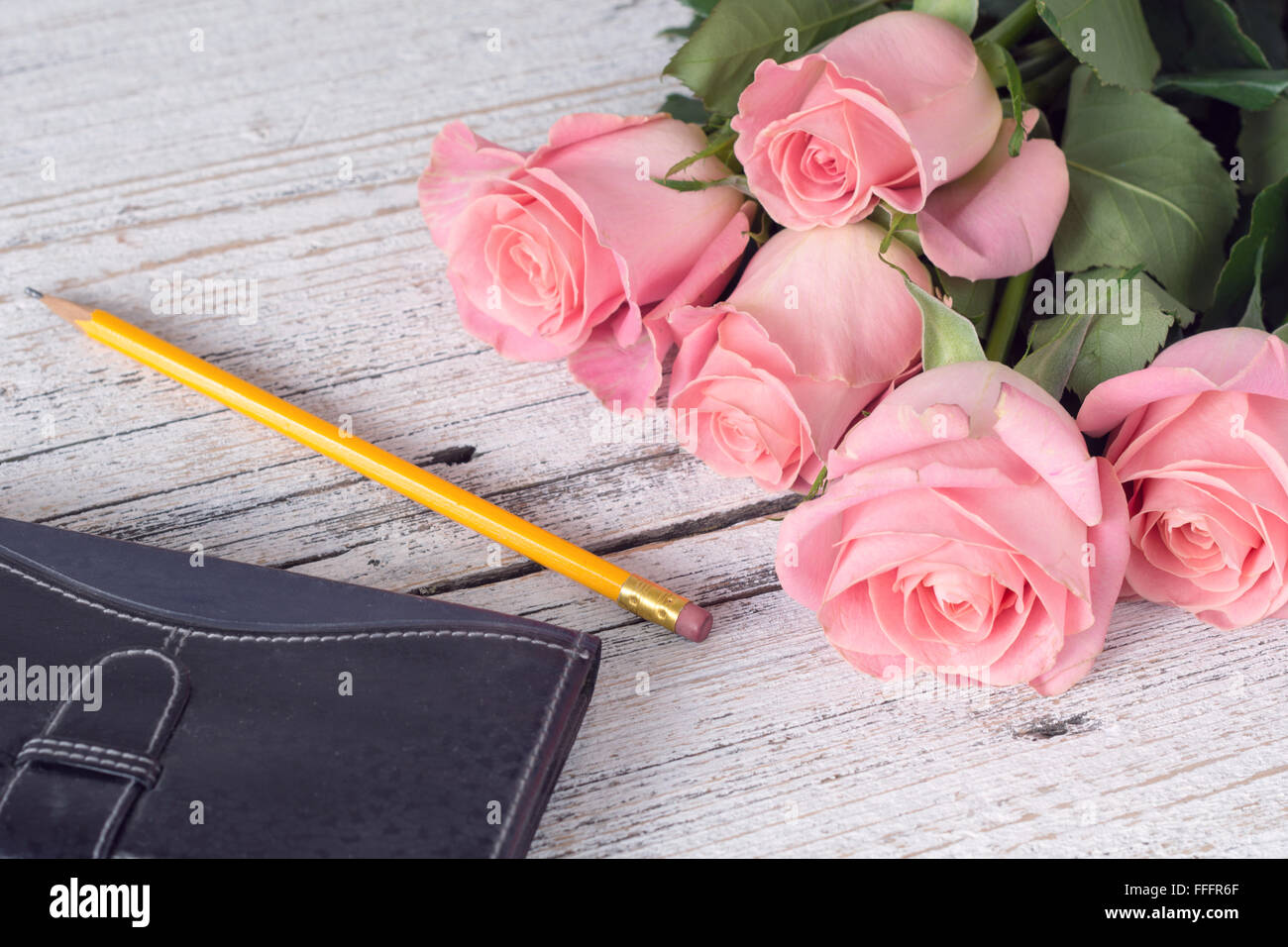 Vintage-Hintergrund / Postkarte / Grusskarte. Rosa Rosen, Notizblock und Bleistift auf weißem strukturierten hölzernen Hintergrund. Nahaufnahme Stockfoto