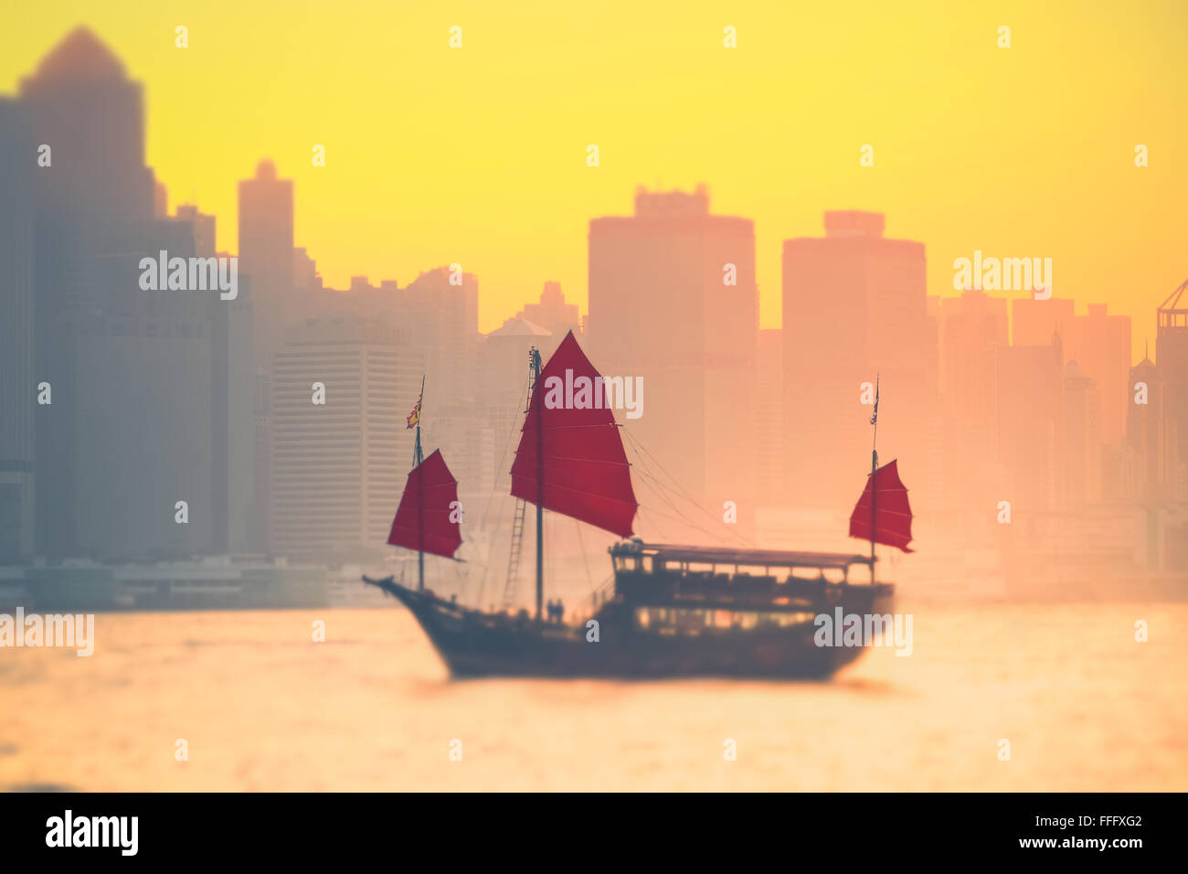 Tilt Shift-Unschärfe-Effekt. Sonnenuntergang Skyline von Hong Kong mit traditionellen Kreuzfahrt-Segelboot im Hafen von Victoria Stockfoto