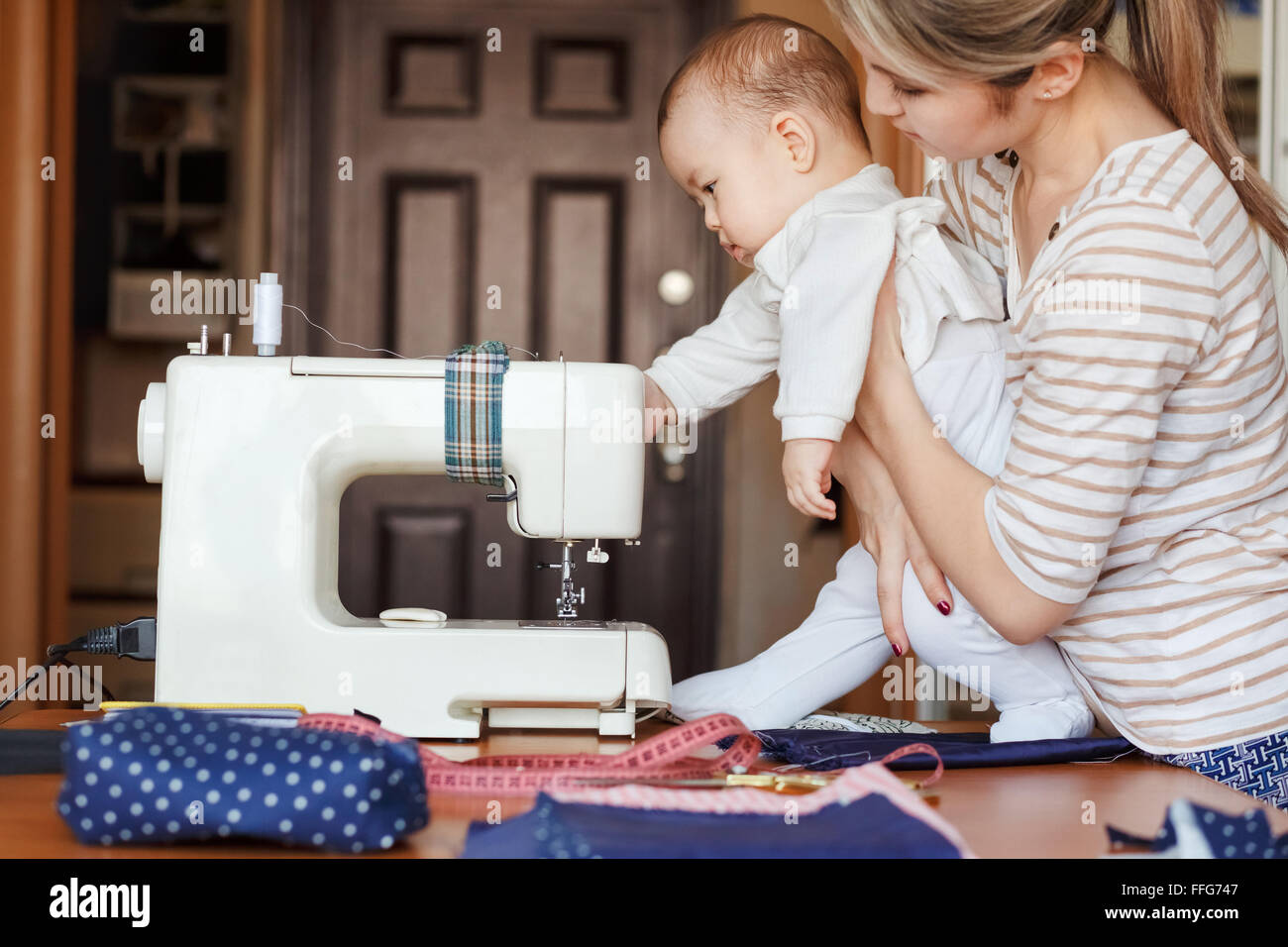 Kleines Kind lernt neuen Erkenntnisse, zusammen mit seiner Mutter inspiziert Nähmaschine. Arbeiten Sie zu Hause, Erziehung, Eltern und Kinder, Betreuung, Babysitter. Stockfoto