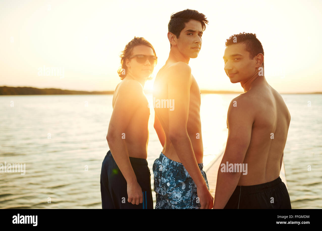 Drei Jungs Im Teenageralter Geniessen Sie Einen Sonnenuntergang Zusammen Stehend Mit Blick Auf Einen Ruhigen See Biegen Sie An Der Kamera Uber Ihre Umhangeta Schauen Stockfotografie Alamy