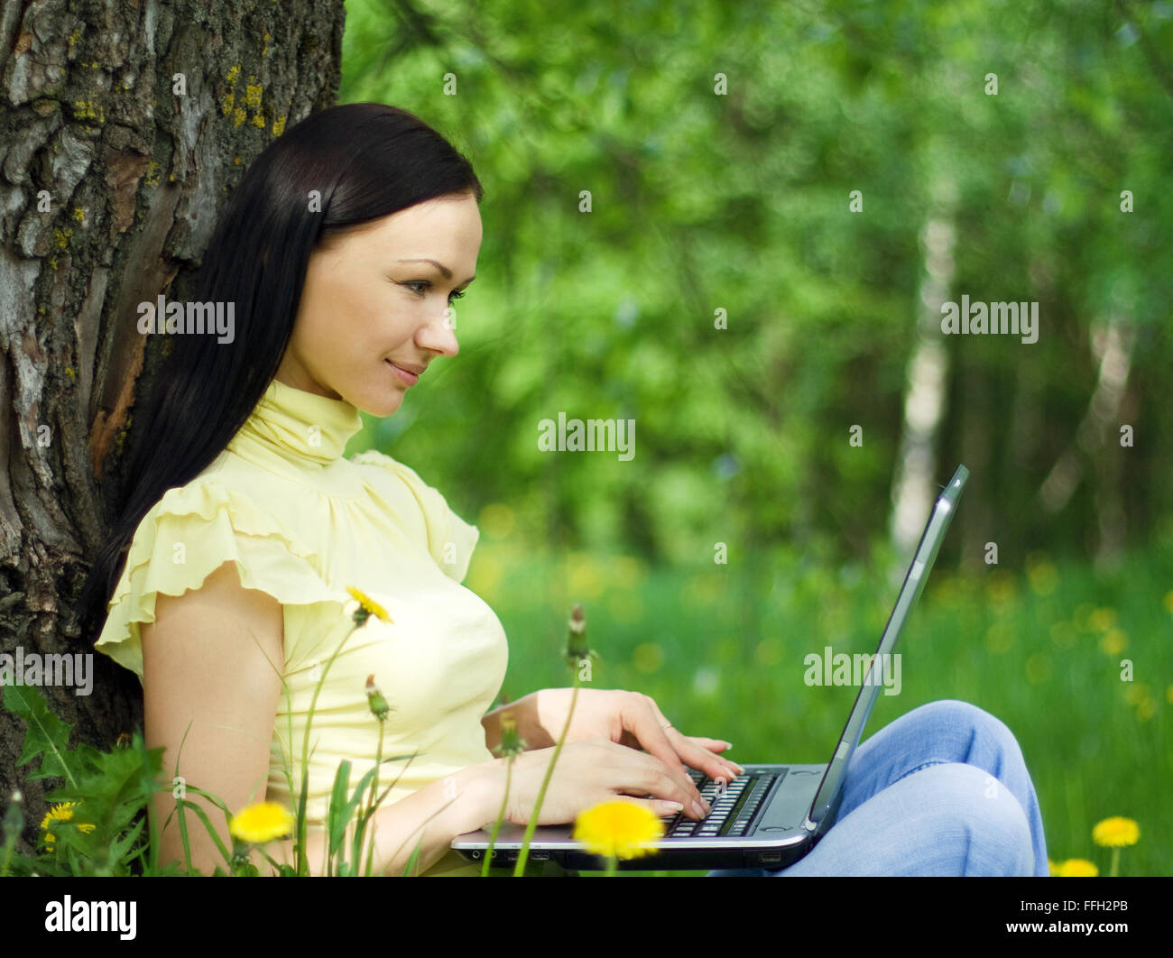 Junge Frau sitzt auf dem Rasen mit Laptop auf den Knien. Stockfoto