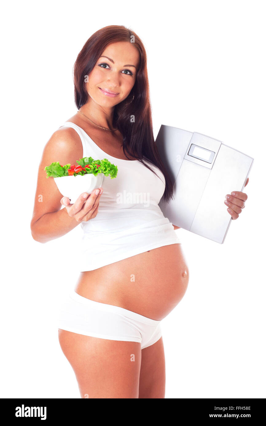 Schwangere Frau mit Skalen in einer Hand zu einem anderen Salat, isoliert auf weiss. Stockfoto