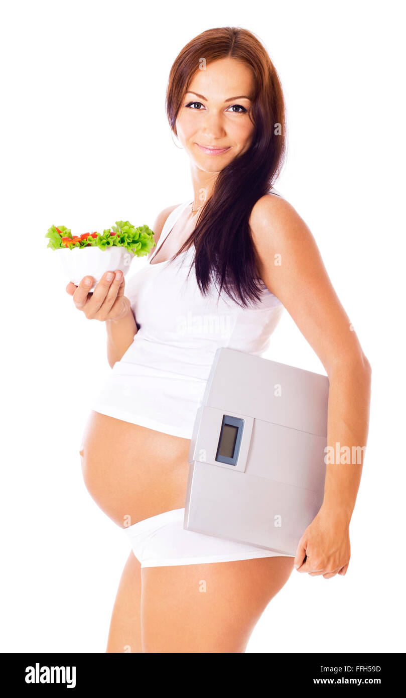 Schwangere Frau mit Skalen in einer Hand zu einem anderen Salat, isoliert auf weiss. Stockfoto