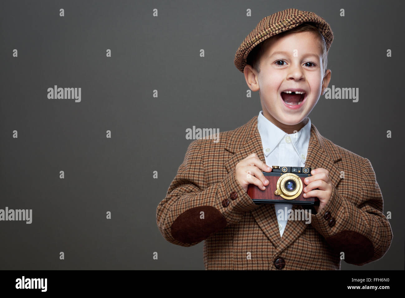 Netter Junge mit Vintage Foto-Kamera auf dem grauen Hintergrund. (Retro-Stil). Stockfoto