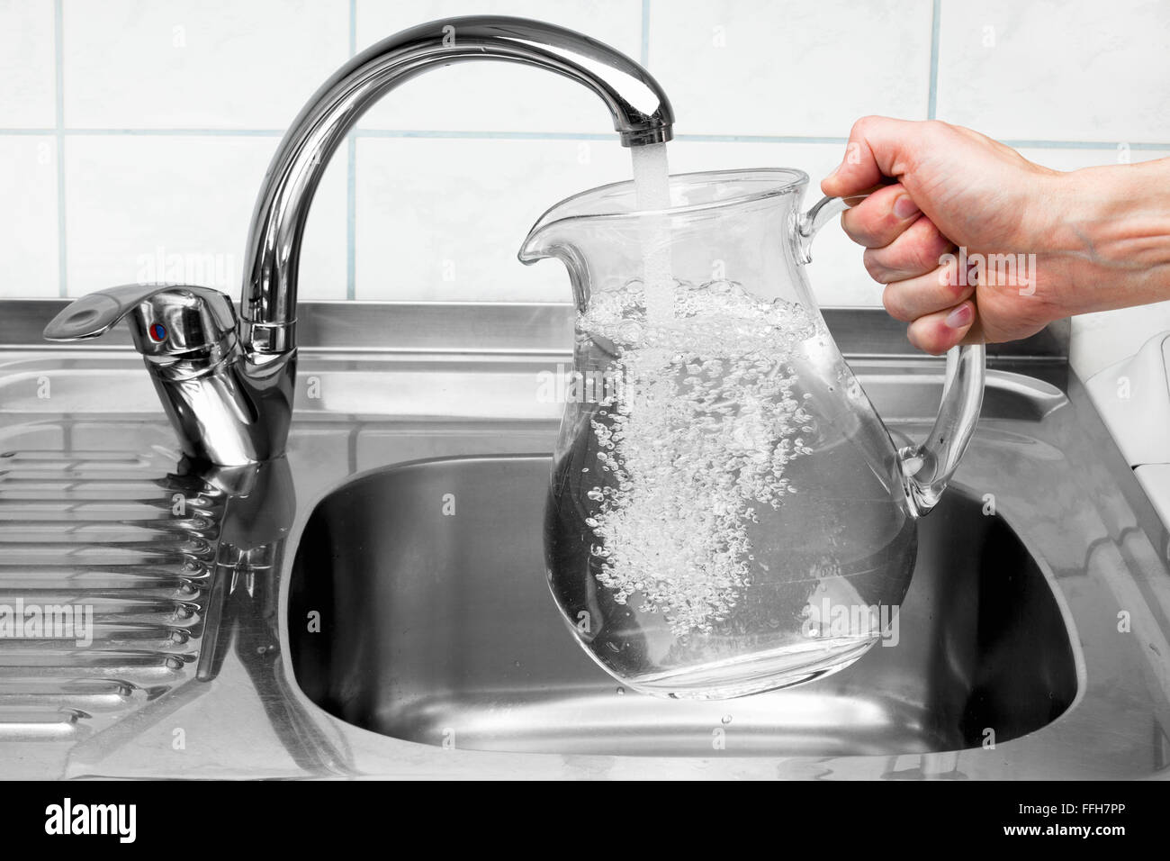 Hand hält einen Krug mit Wasser aus der Küchenarmatur gegossen wird. Stockfoto