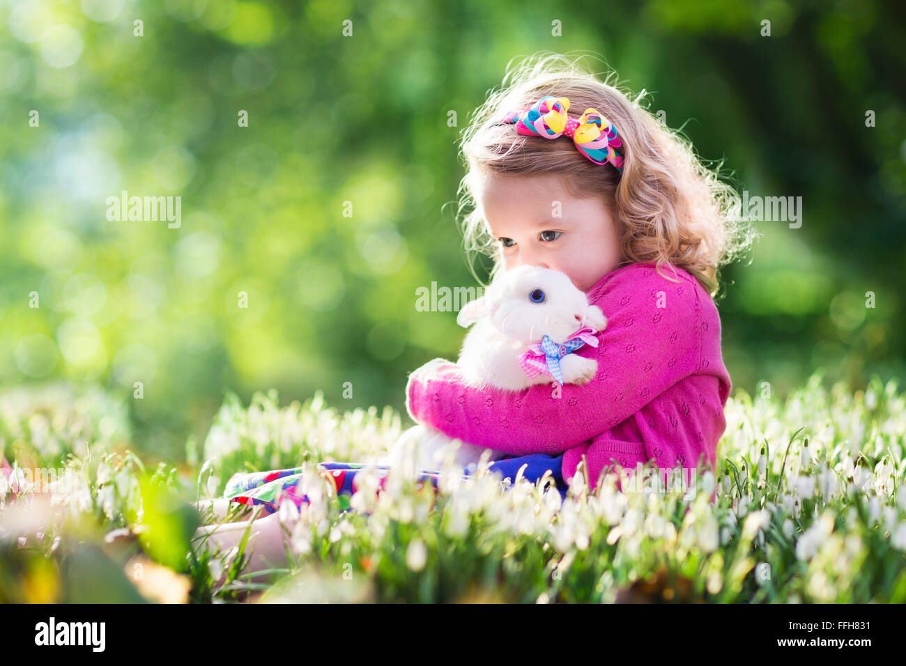 Niedlichen Kleinkind Mädchen spielen mit echten Hasen in blühenden Frühling Garten. Kind auf Ostereiersuche. Kind mit bunten Eiern und streicheln Stockfoto