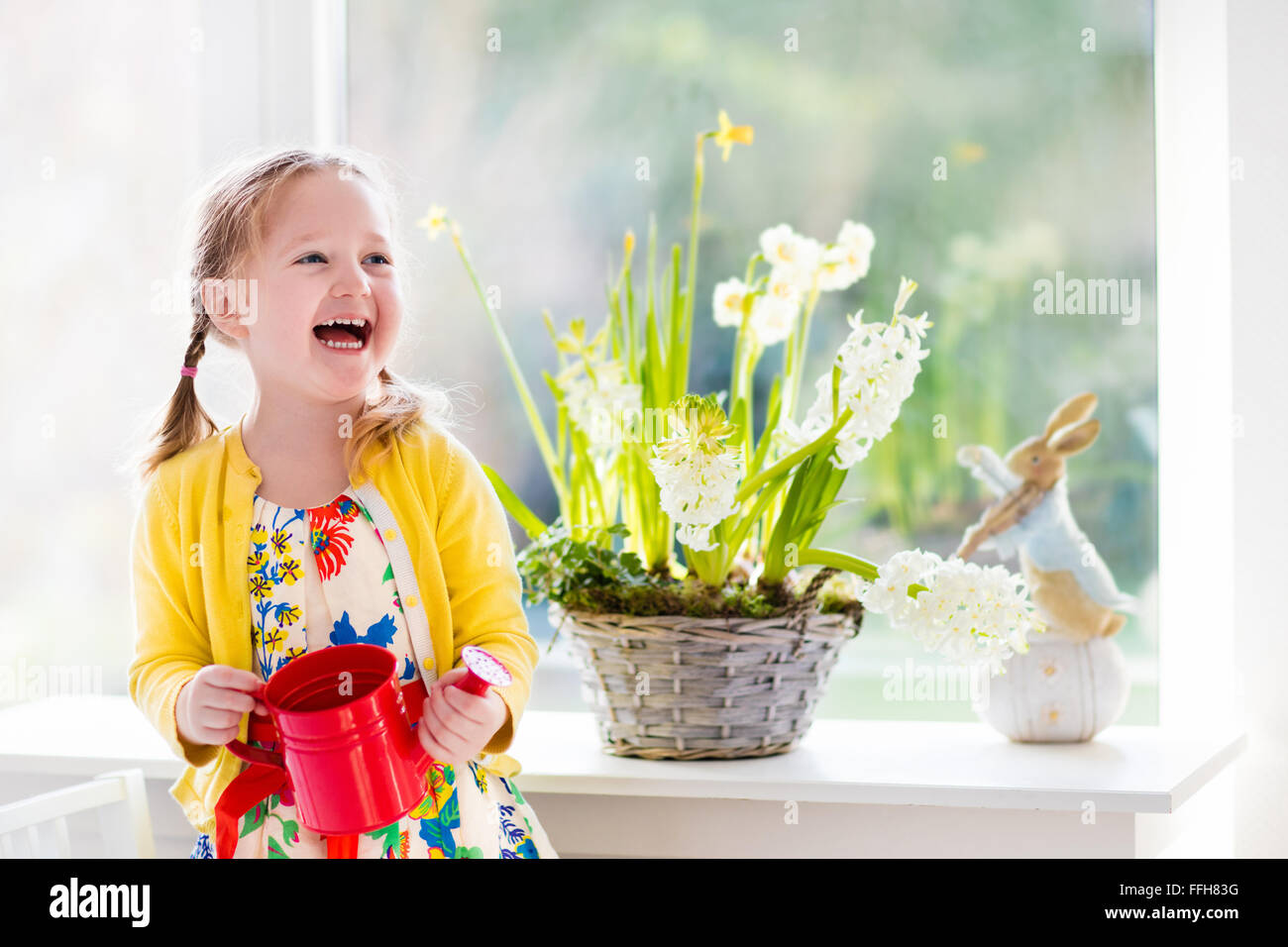 Niedliche Mädchen erste Frühlingsblumen gießen. Ostern-Wohngebäude und Dekoration. Kind kümmert sich um Pflanzen. Kind mit Wasser kann. Stockfoto
