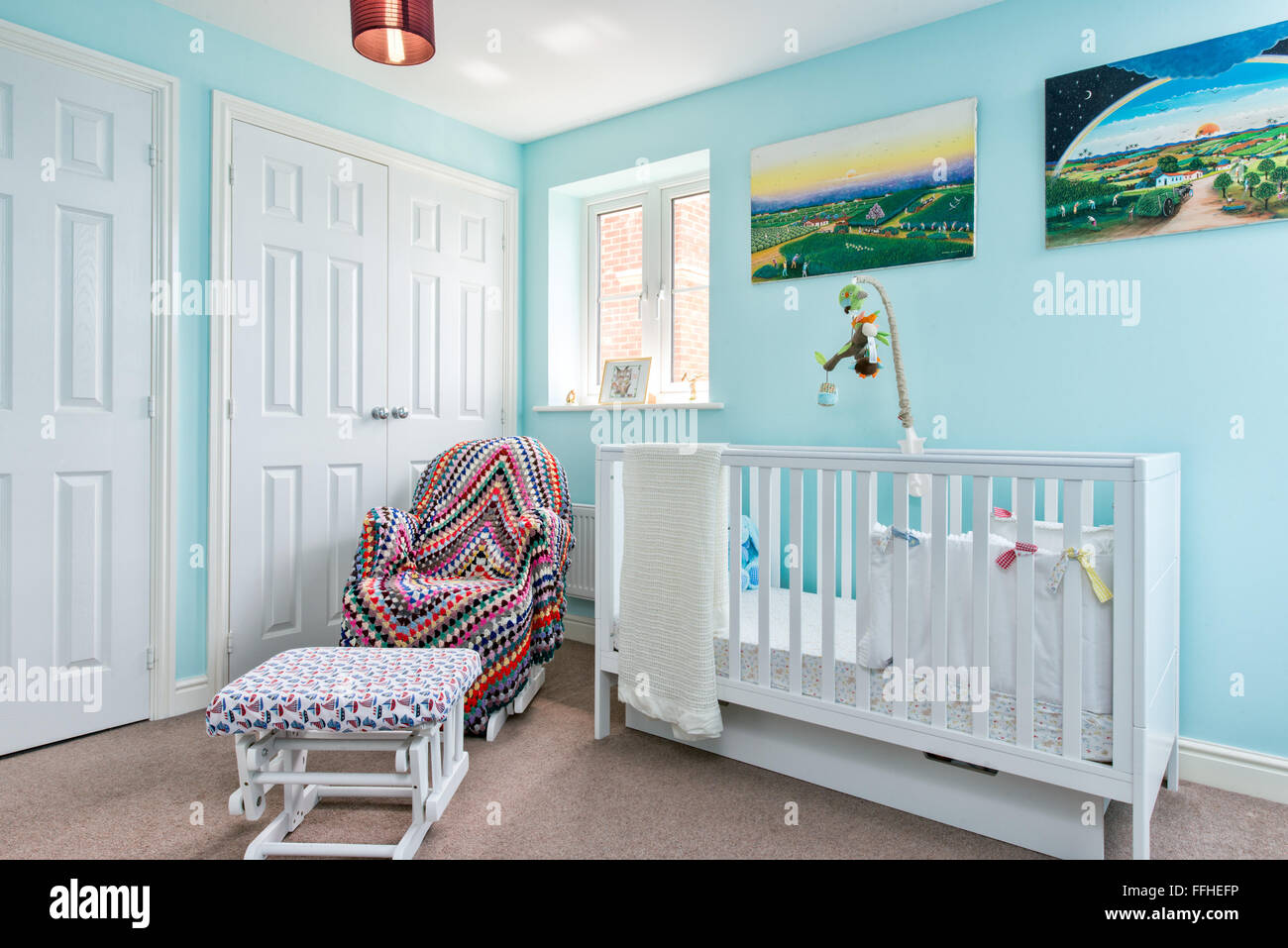 Die Kinderstube der ein kleines Kind in blau & weiß mit einem Kinderbett eingerichtet und Krankenpflege Stuhl bedeckt mit einem Wurf Stockfoto