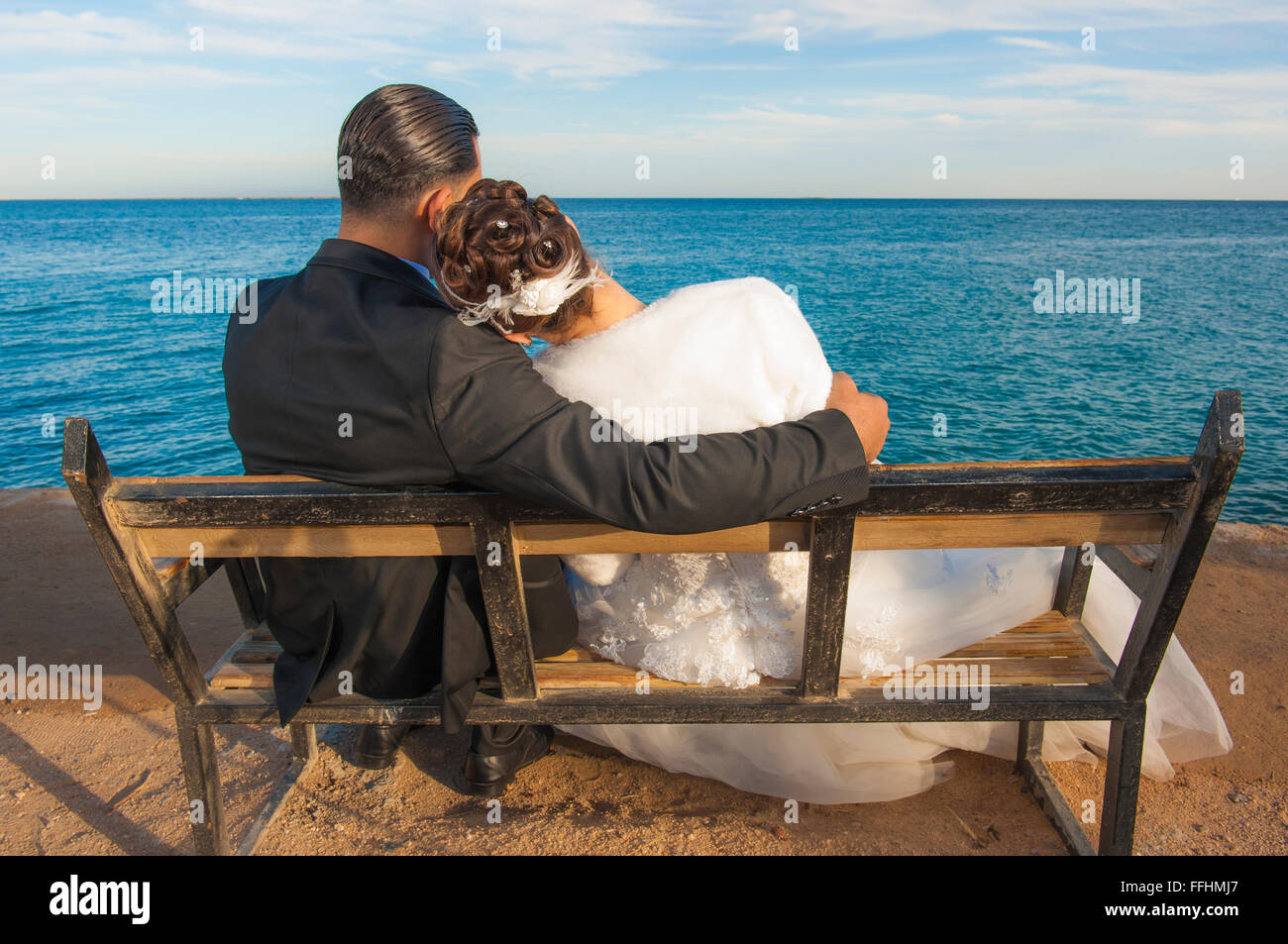 Braut und Bräutigam Paar sitzt auf einer Holzbank mit Blick auf tropische Meer Stockfoto