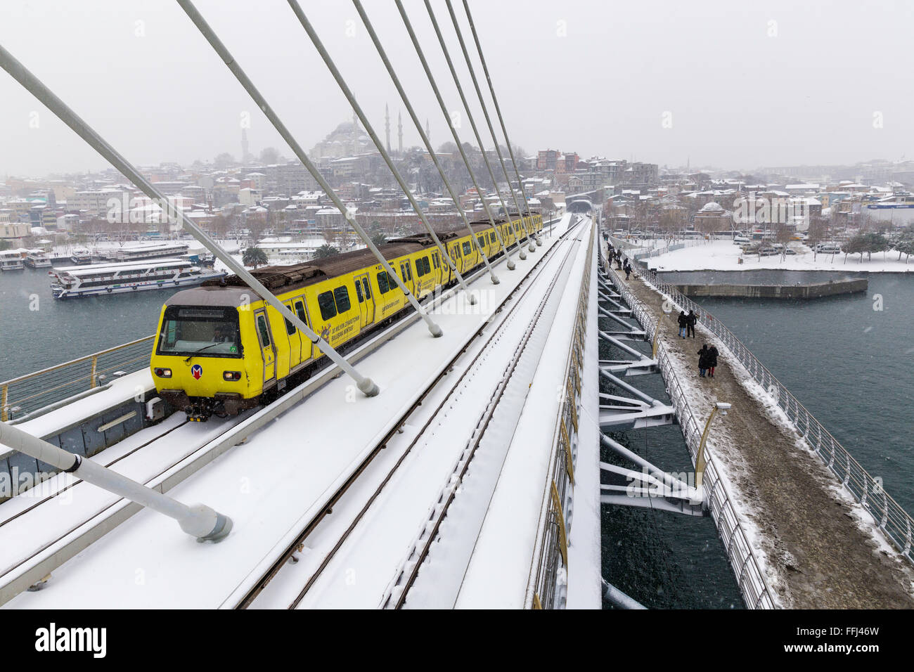 Istanbul u-Bahn u-Bahn Zug vorbei und Menschen zu Fuß auf das Goldene Horn U-Bahn Brücke an einem verschneiten Tag in der Nähe von Halic in Istanbul Stockfoto