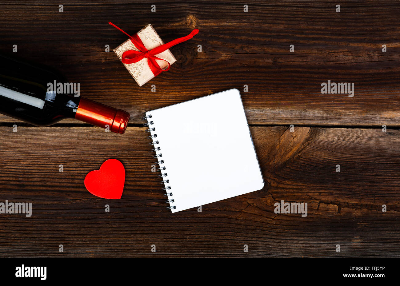 Rotes Herz aus Holz, Flasche Wein, Geschenk-Box und Notizblock auf alten Holzbrett. Liebe-Konzept. Valentinstag Hintergrund. Stockfoto