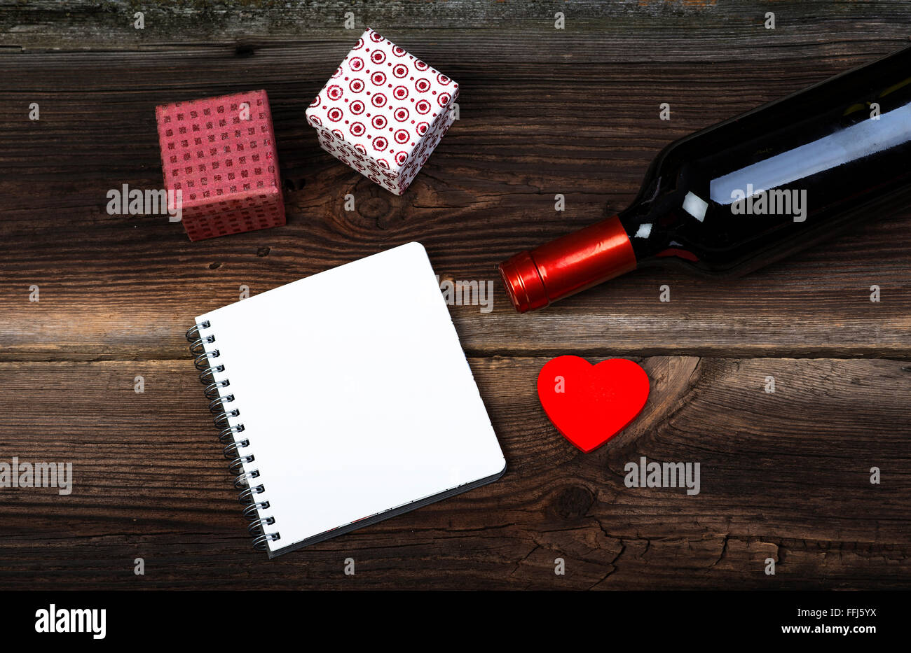 Rotes Herz aus Holz, Flasche Wein, Geschenk-Boxen und Notizblock auf Holzbrett. Liebe-Konzept. Valentinstag Hintergrund. Stockfoto