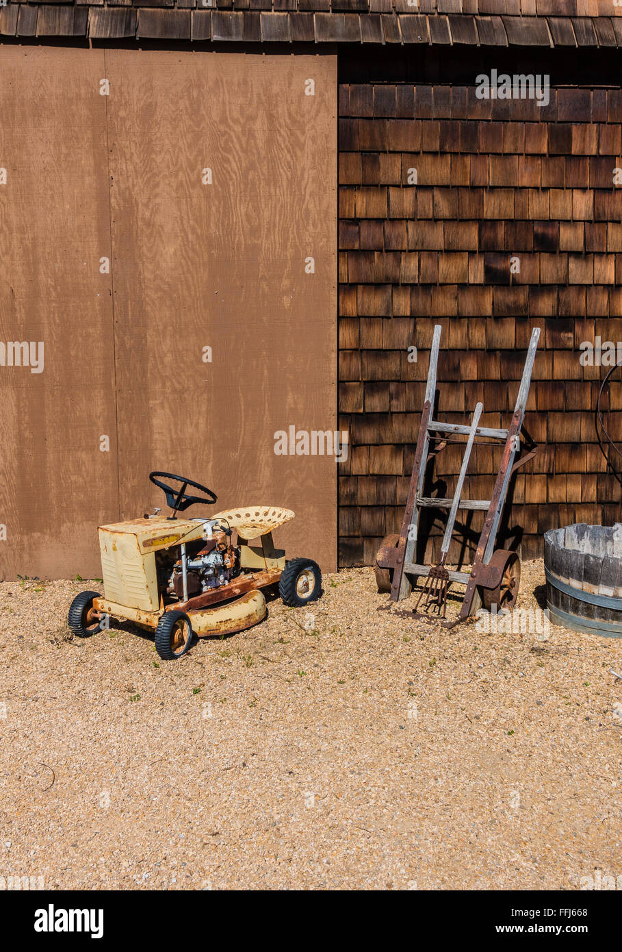 Farm Equipment Stilleben vor ein landwirtschaftliches Gebäude mit einem kleinen vierrädrigen Traktor, antike zwei Rädern Sackkarre platziert. Stockfoto