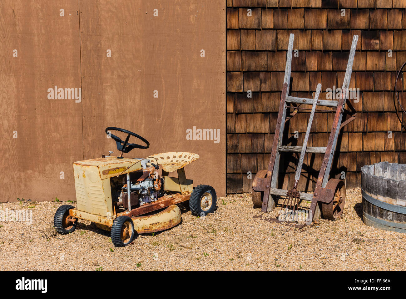 Farm Equipment Stilleben vor ein landwirtschaftliches Gebäude mit einem kleinen vierrädrigen Traktor, antike zwei Rädern Sackkarre platziert. Stockfoto