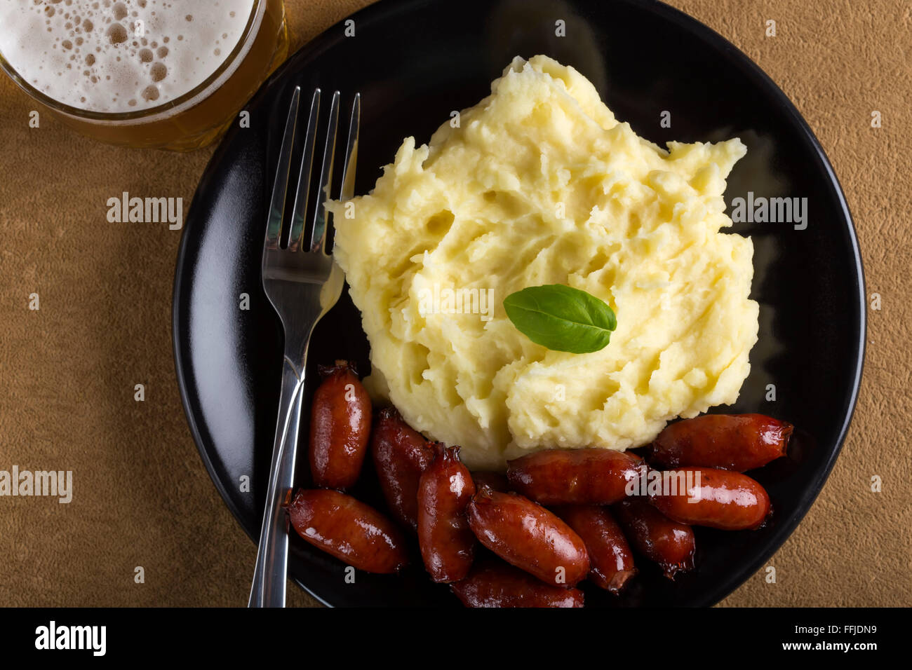 Kartoffelbrei mit Fleischwurst auf Teller mit Gabel und ein Glas Bier Stockfoto