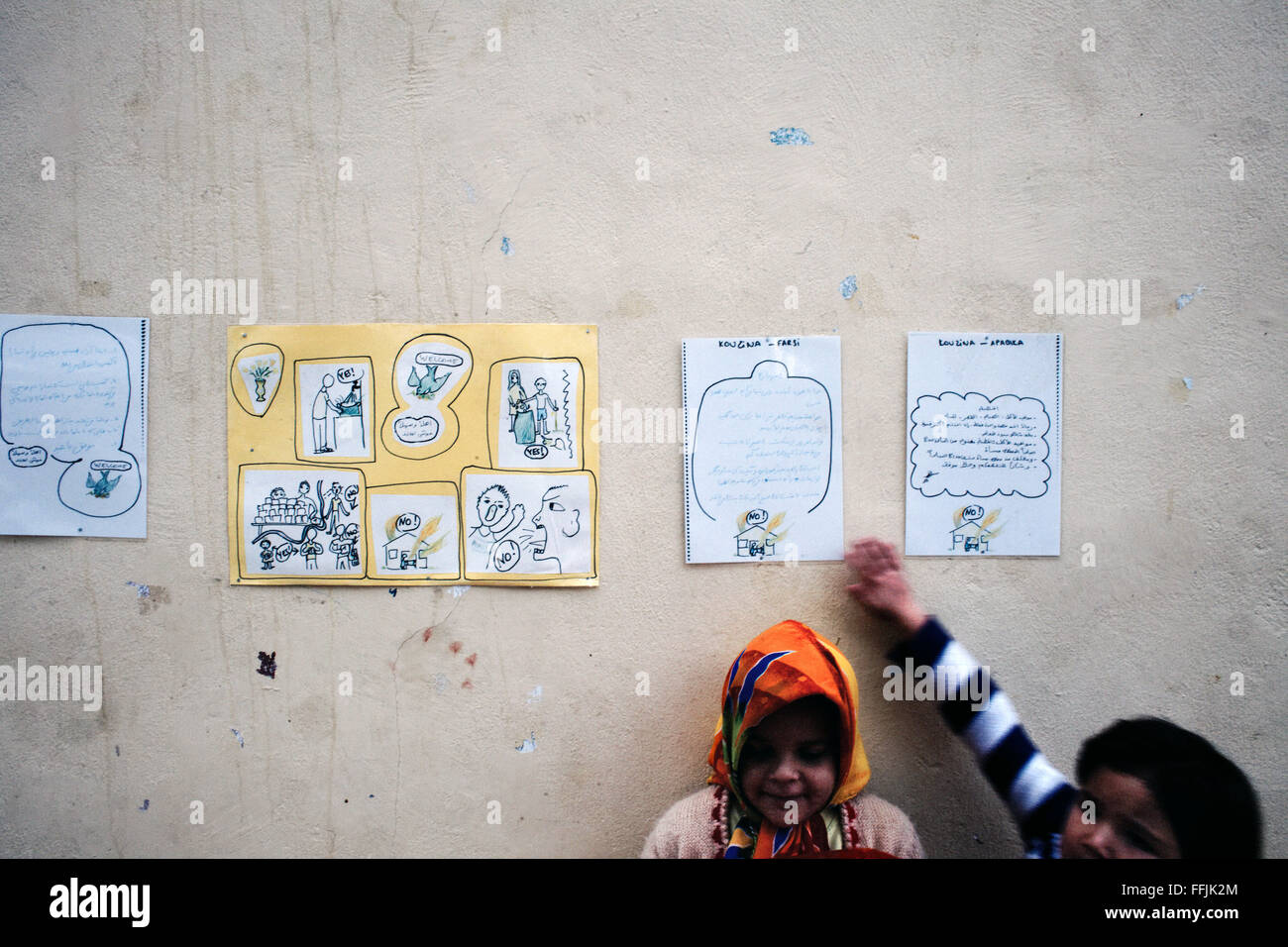 Kinder spielen vor der Wand wo angeheftet sind die Regeln für die Nutzung der Küche in Arabisch und Persisch im Pikpa-Dorf Stockfoto