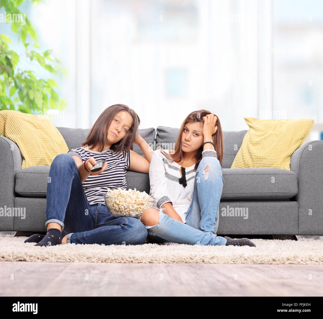 Zwei gelangweilte teenage Mädchen vor dem Fernseher sitzen auf dem Boden vor einem grauen Sofa zu Hause Schuss mit Tilt-Shift-Objektiv Stockfoto