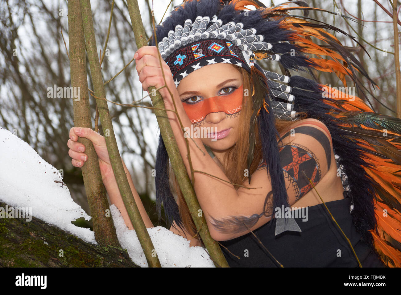Mädchen in Indianer Kopfschmuck auf dem Baum im Winterwald Stockfoto