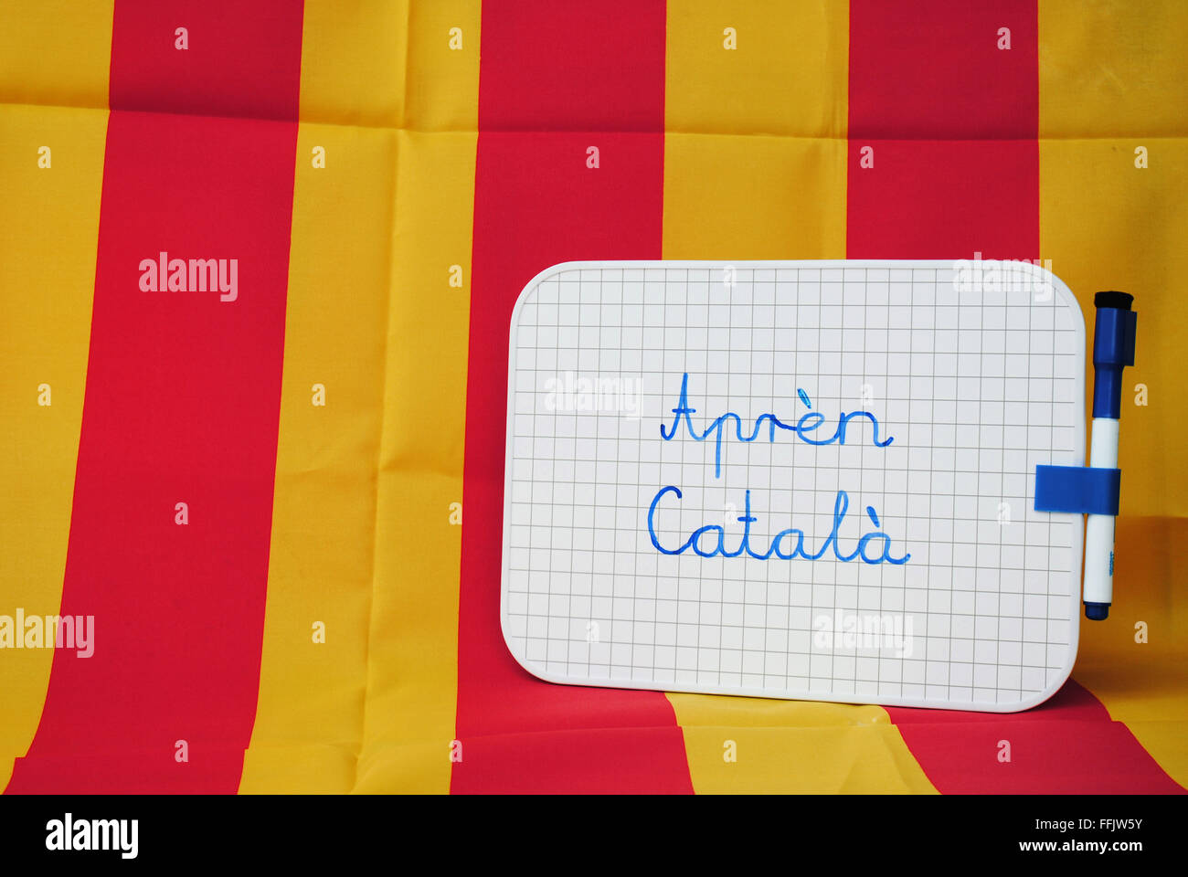 "Katalanisch auf Katalanisch lernen" geschrieben auf einem kleinen Whiteboard gegen eine gelb und rot - Hintergrund katalanische Flagge. Stockfoto
