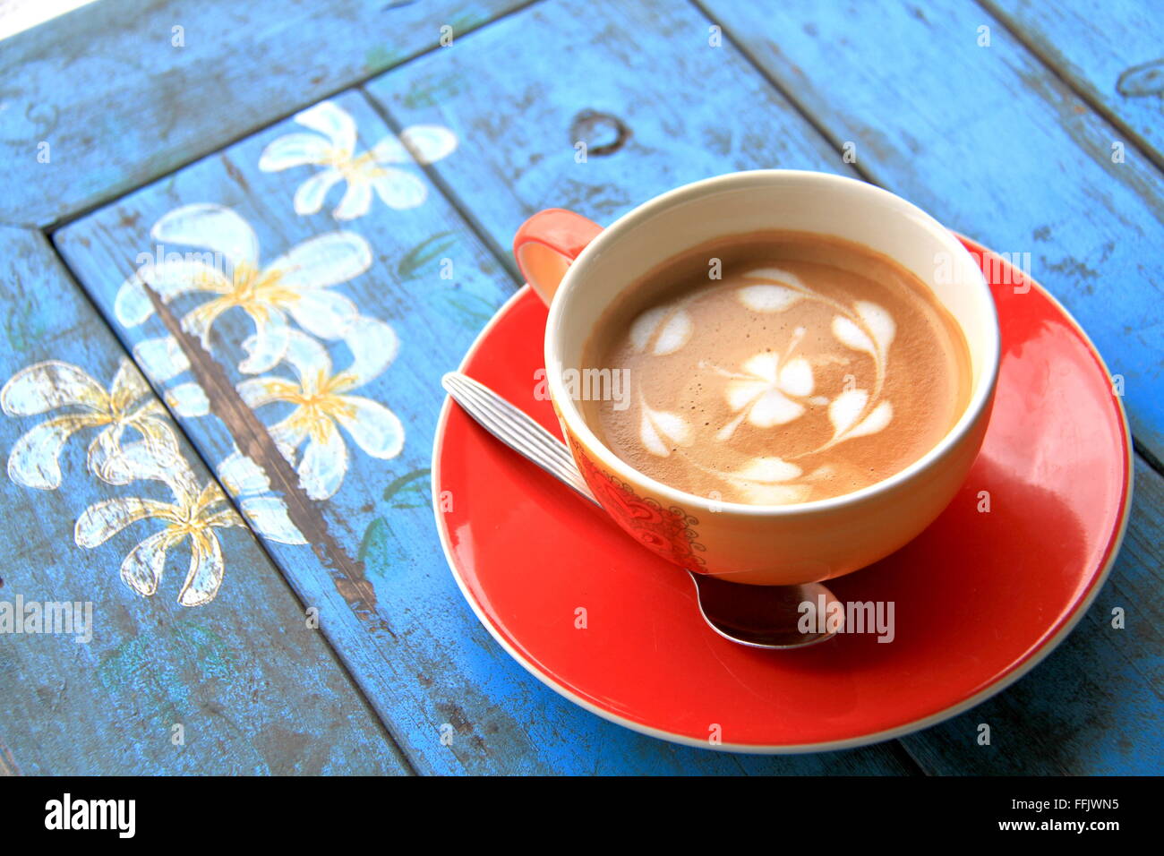 Rote Tasse Kaffee mit Herz und Blume gemalt auf Schaum auf schmutzigen blaue Tabelle Stockfoto