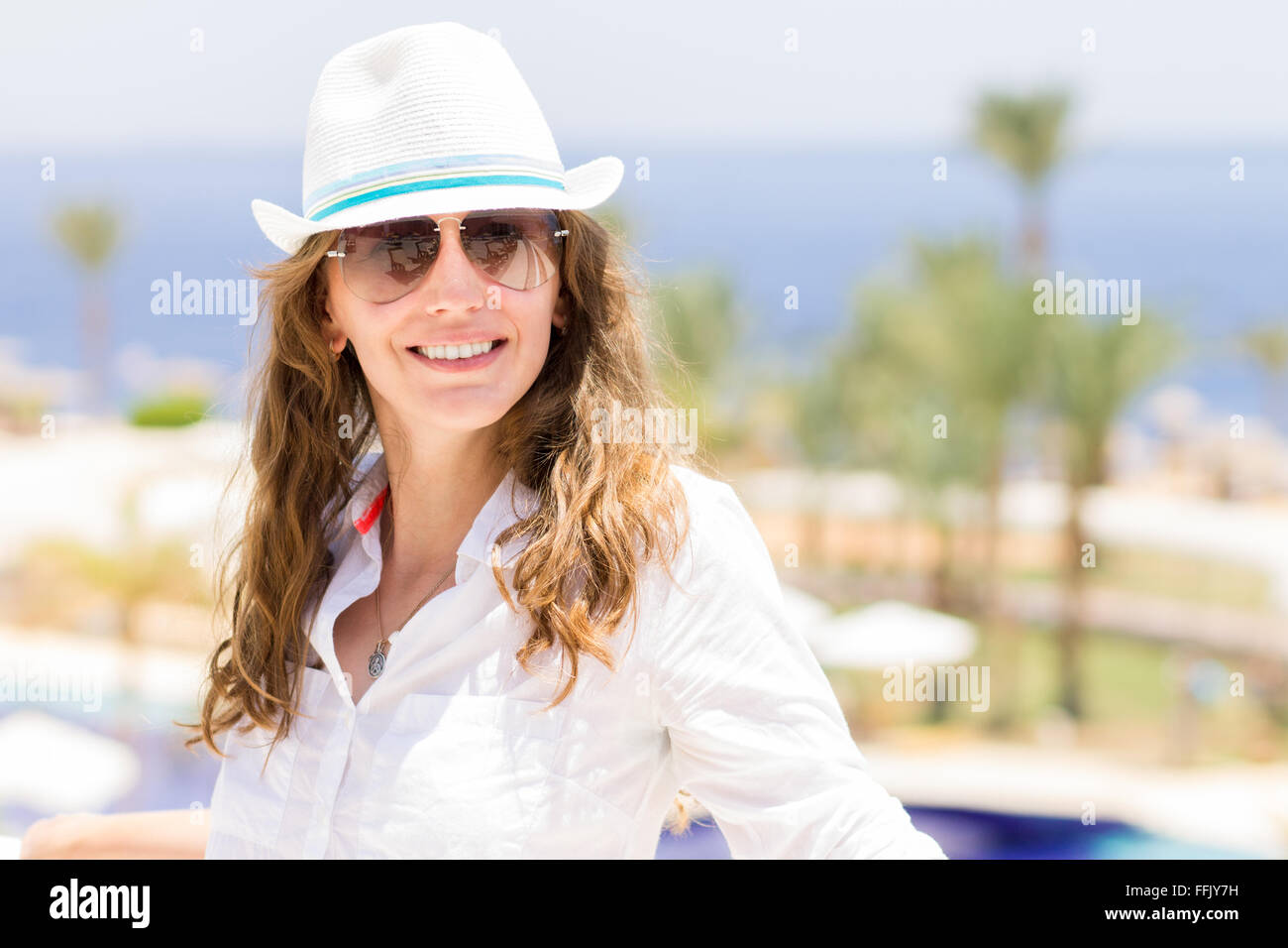 Junge europäische lächelnde Frau in weißem Hemd und Hut im tropischen Resort. Sommer Urlaub Hintergrund mit glückliches Mädchen Stockfoto