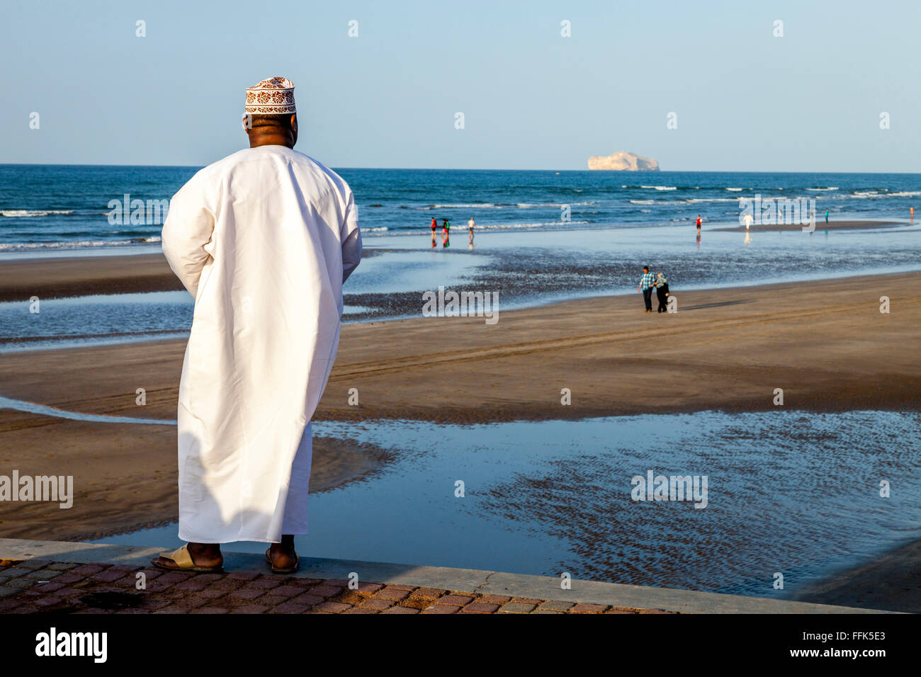 Ein omanischer Mann In traditioneller Kleidung blickt über den Strand von Muscat, Sultanat von Oman Stockfoto