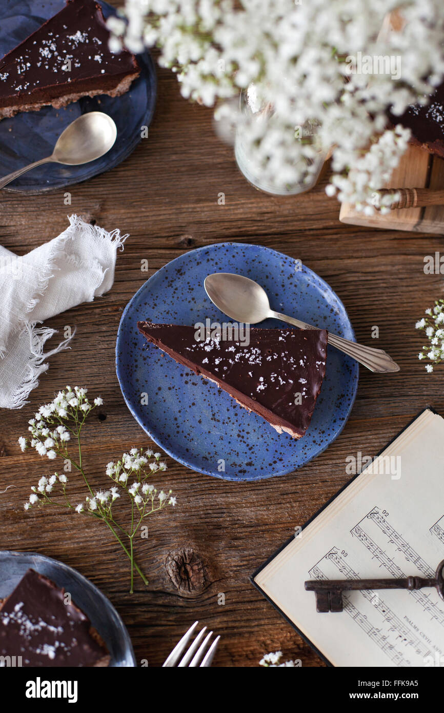 Schokoladen-Tarte Scheiben auf Tellern und Blumen auf einem rustikalen Holztisch Stockfoto