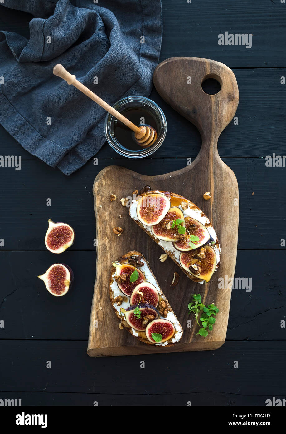 Sandwiches mit Ricotta, frische Feigen, Walnüssen und Honig auf rustikalem Holzbrett auf schwarzem Hintergrund, Ansicht von oben Stockfoto