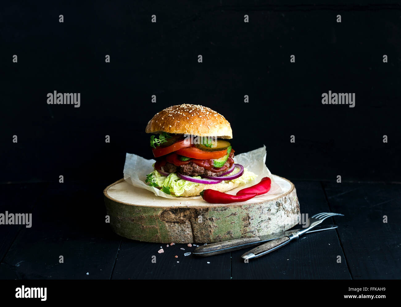 Frische hausgemachte Burger auf hölzernen Portion Brett mit würziger Tomatensauce, Meersalz und Kräutern auf schwarzem Hintergrund Stockfoto