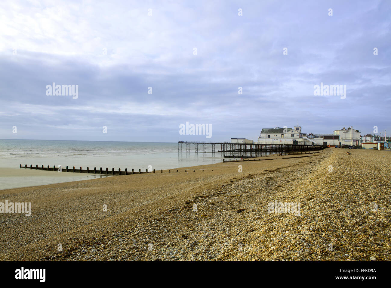 Die Flut ist draußen so ein Schuss Blick entlang des Strandes auf den viktorianischen Pier über dem Kiesstrand. Stockfoto