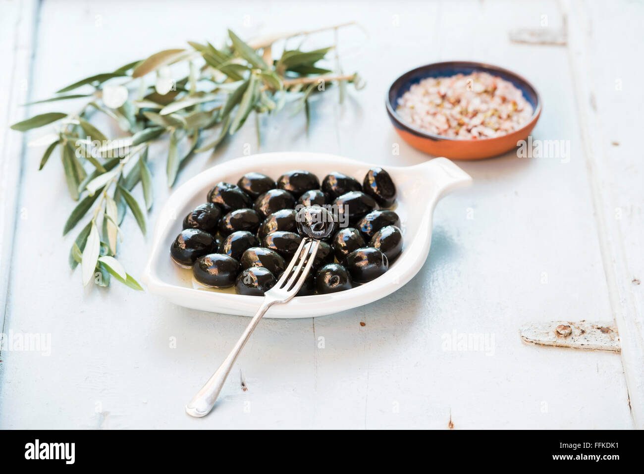 Schwarze Oliven in weißen Keramikplatte, Zweige und Gewürzen über hellblauen Hintergrund, selektiven Fokus Stockfoto