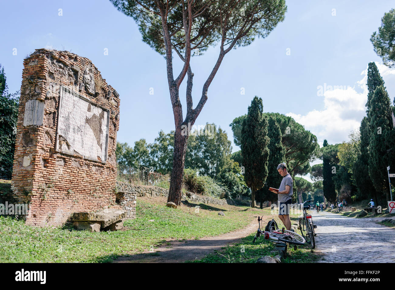 Ein männlicher Tourist mit seinem Fahrrad anzuhalten, ein historisches Denkmal auf der Via Appia zu bewundern / Via Appia in Rom, Italien. Stockfoto
