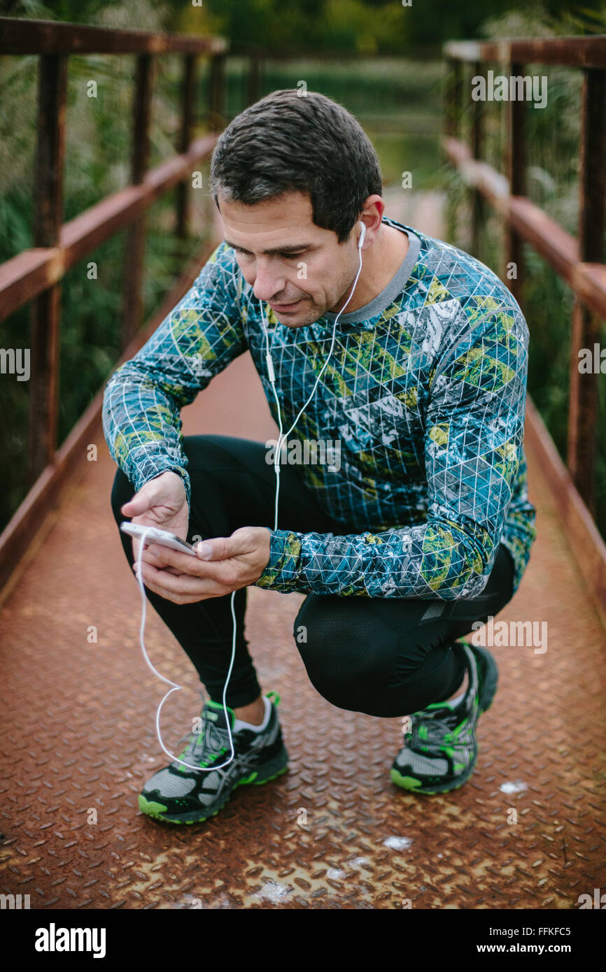 Läufer auf rostigen Brücke mit Smartphone Musik hören Stockfoto