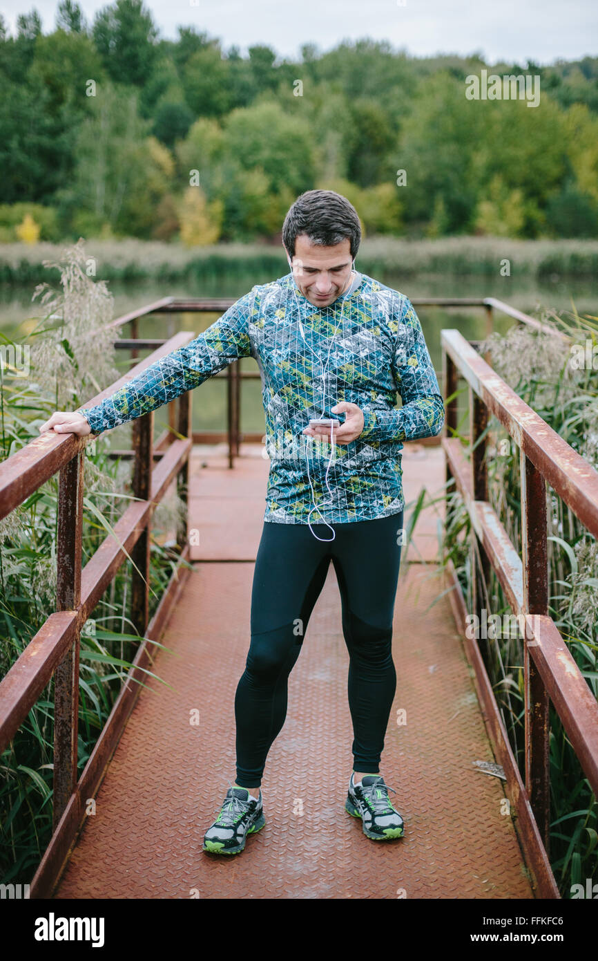 Läufer auf rostigen Brücke mit Smartphone gegen die grüne Natur Stockfoto