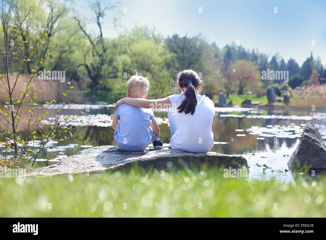 Urlaub-Zeit am Wasser entspannen. Zwei Kinder, ältere Schwester und Bruder sitzen am Ufer des Sees Stockfoto