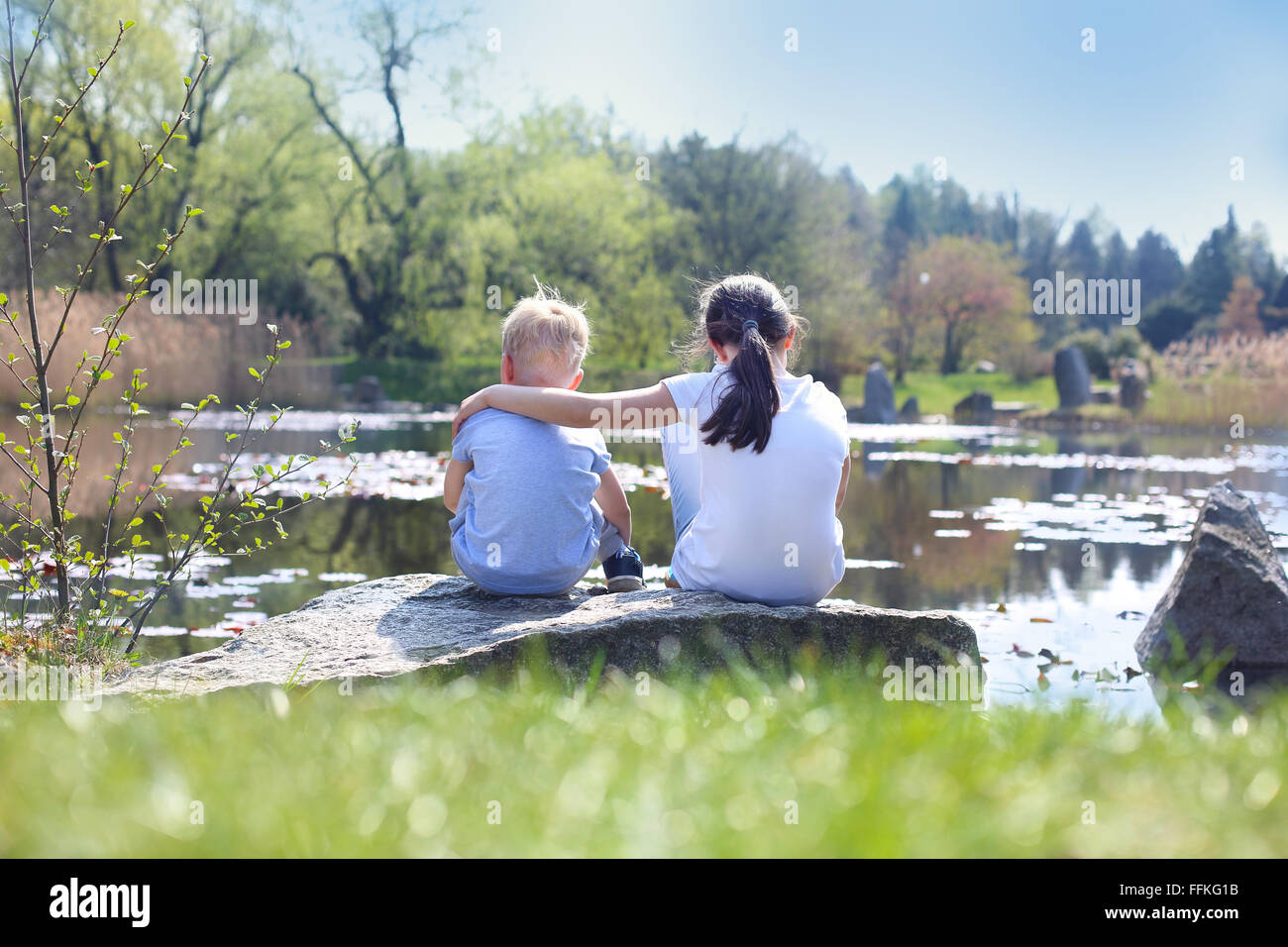 Urlaub-Zeit am Wasser entspannen. Zwei Kinder, ältere Schwester und Bruder sitzen am Ufer des Sees Stockfoto