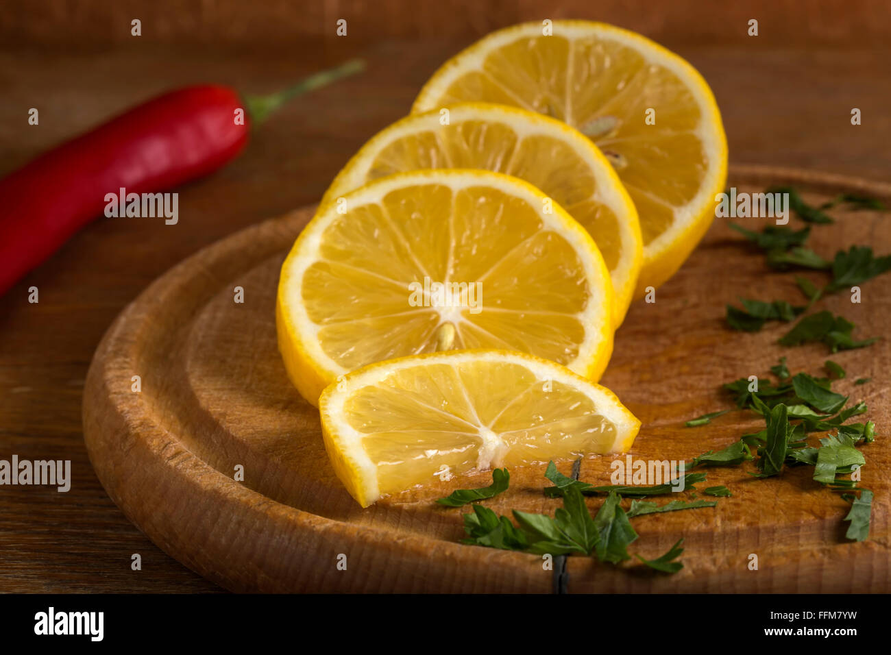 In Scheiben geschnittene Zitrone und rotglühende Chilischote auf dem hölzernen Schneidebrett mit Petersilie Stockfoto