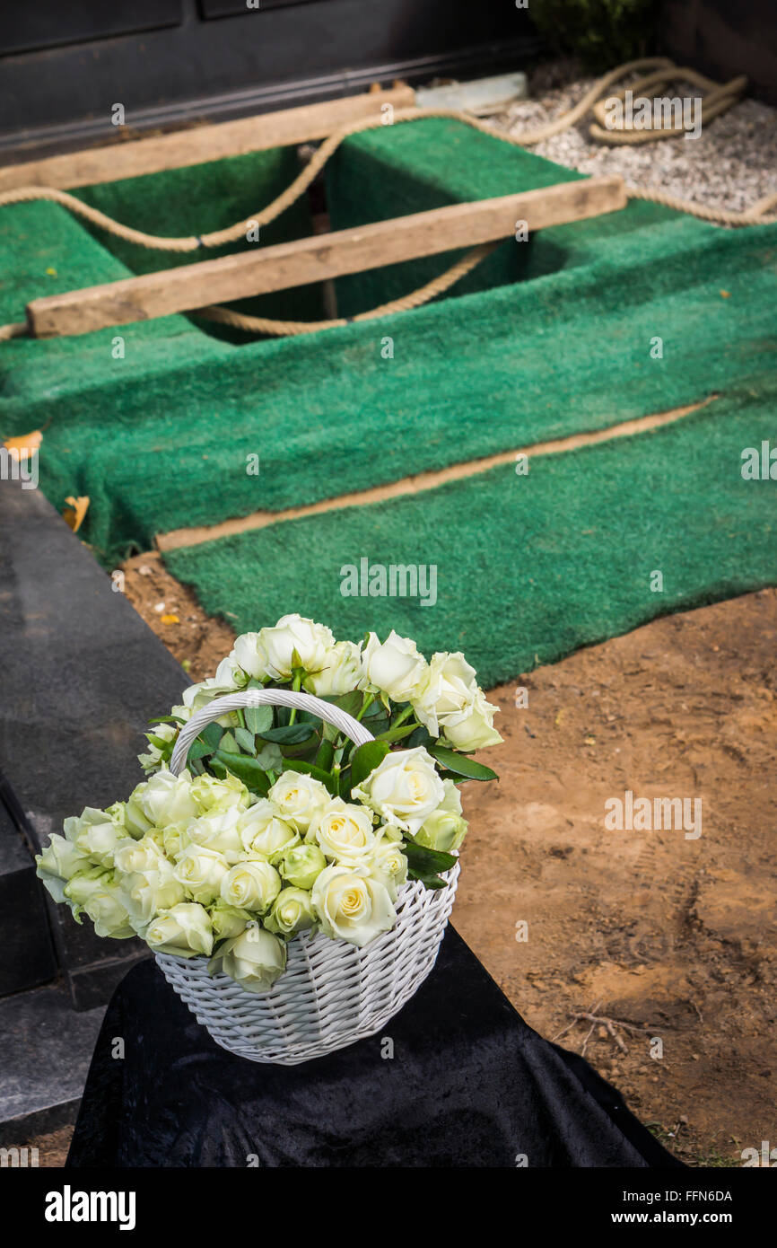 Korb mit weißen Blüten vor einem frisch ausgehobenen Grab Stockfoto