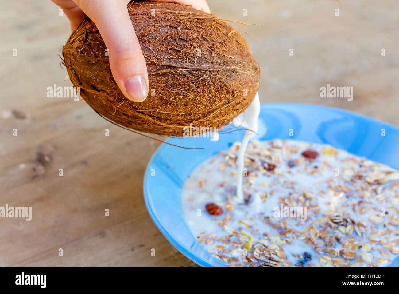 Gießen von einer Kokosnuss Milch in eine Schüssel mit Müsli Müsli Stockfoto