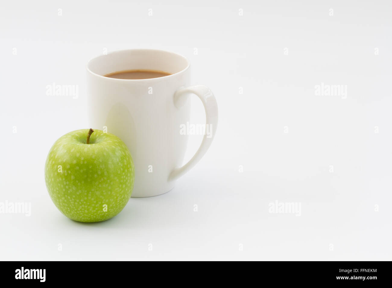 Eine gesunde Arbeitspause, Snacks, ein frischer, grüner Apfel und heiße Tasse Kaffee oder Tee auf einem weißen Hintergrund. Stockfoto