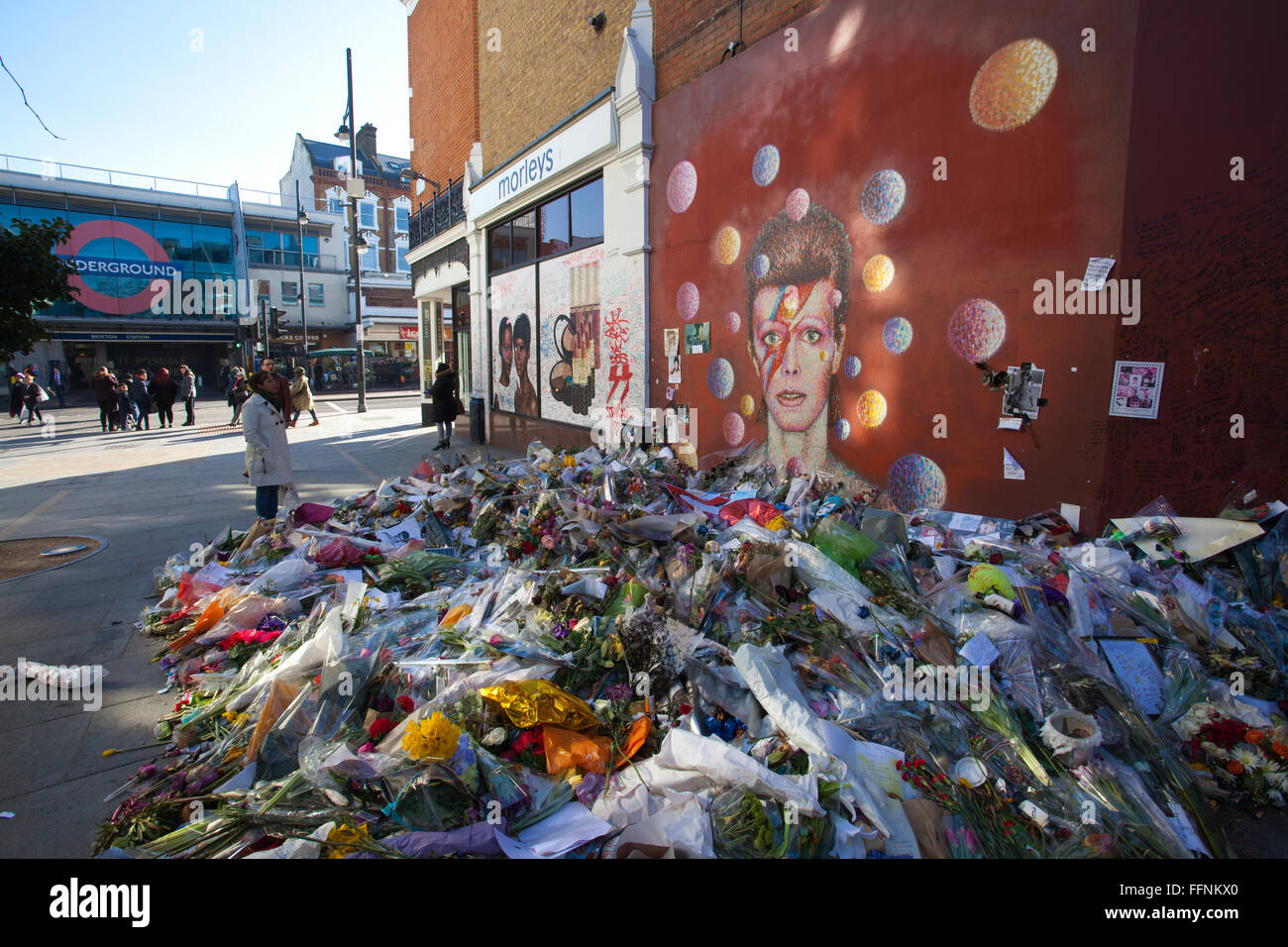 Blumen unter einem David Bowie "Aladdin Sane" Wandbild auf einer Straße Wand in Brixton, nach seinem Tod in einem behelfsmäßigen Schrein gemacht. Stockfoto