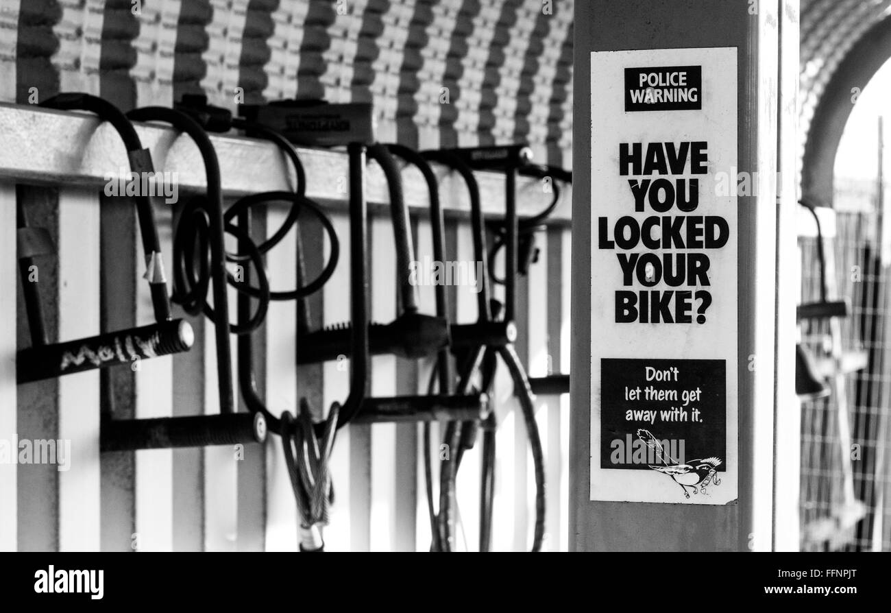 Ein "Haben Sie Ihr Fahrrad gesperrt?" Schild Warnung vor Fahrraddiebstahl vor Fahrradschlösser gesperrt um eine Fahrrad-Unterstand mit keine Fahrräder. Stockfoto